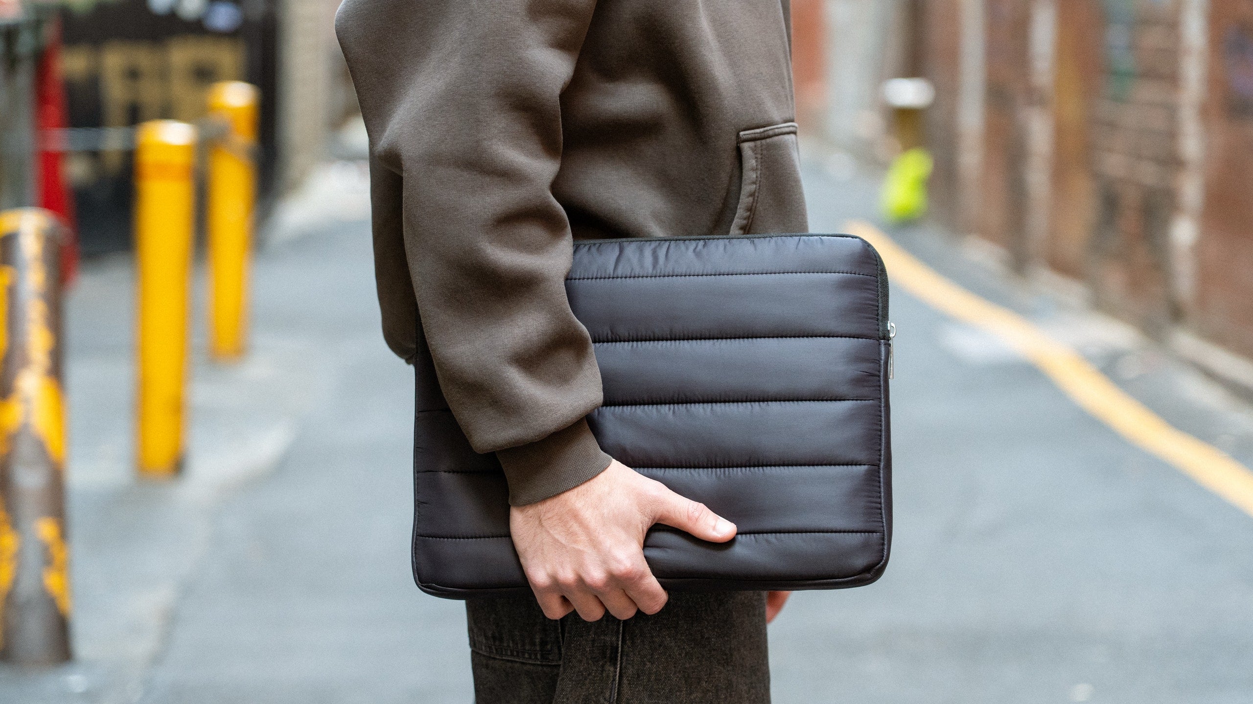 Person carrying a black Humley padded laptop sleeve in an urban alleyway setting