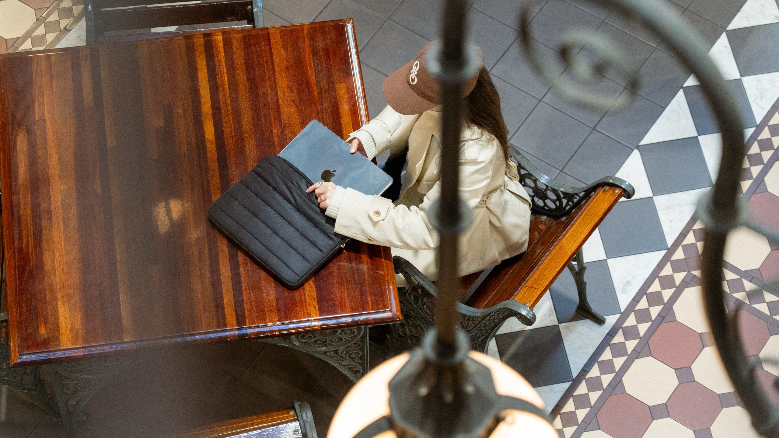 Woman removing MacBook from black Humley padded sleeve at a café-style table with tiled floor