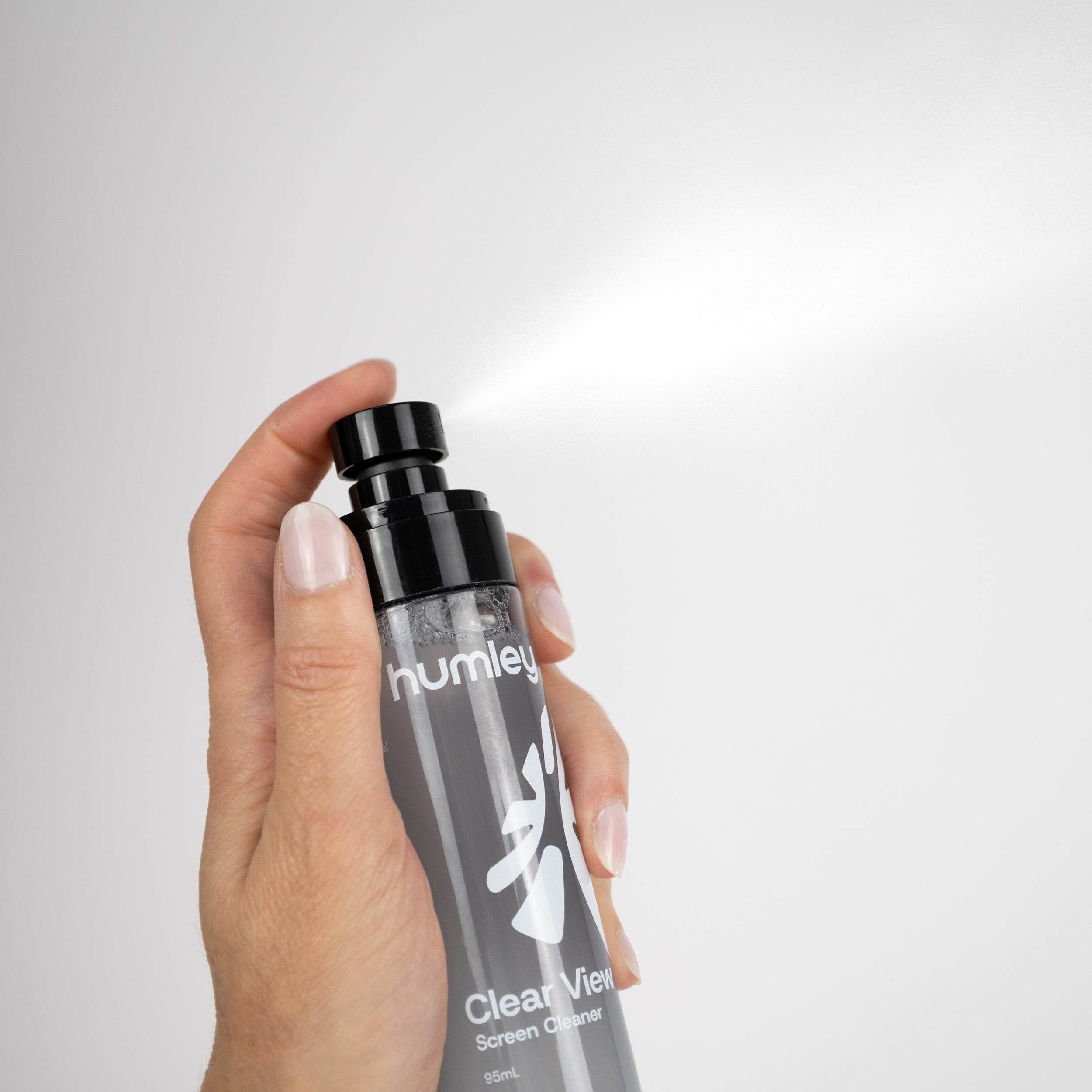 Hand spraying Humley Clear View Screen Cleaner into the air from a black pump bottle.